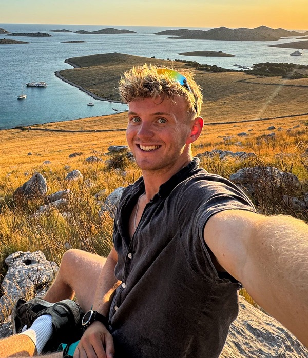 Harry, sitting on a rocky hillside above the sea at sunset