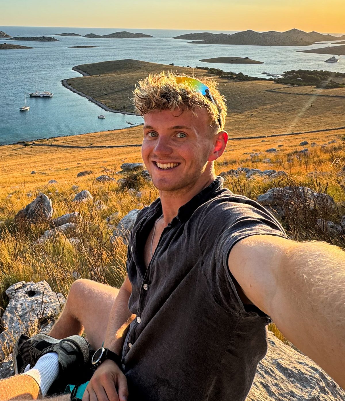 Harry, sitting on a rocky hillside above the sea at sunset